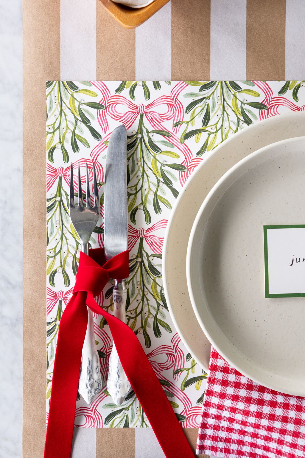 A mistletoe patterned placemat under a holiday place setting. 