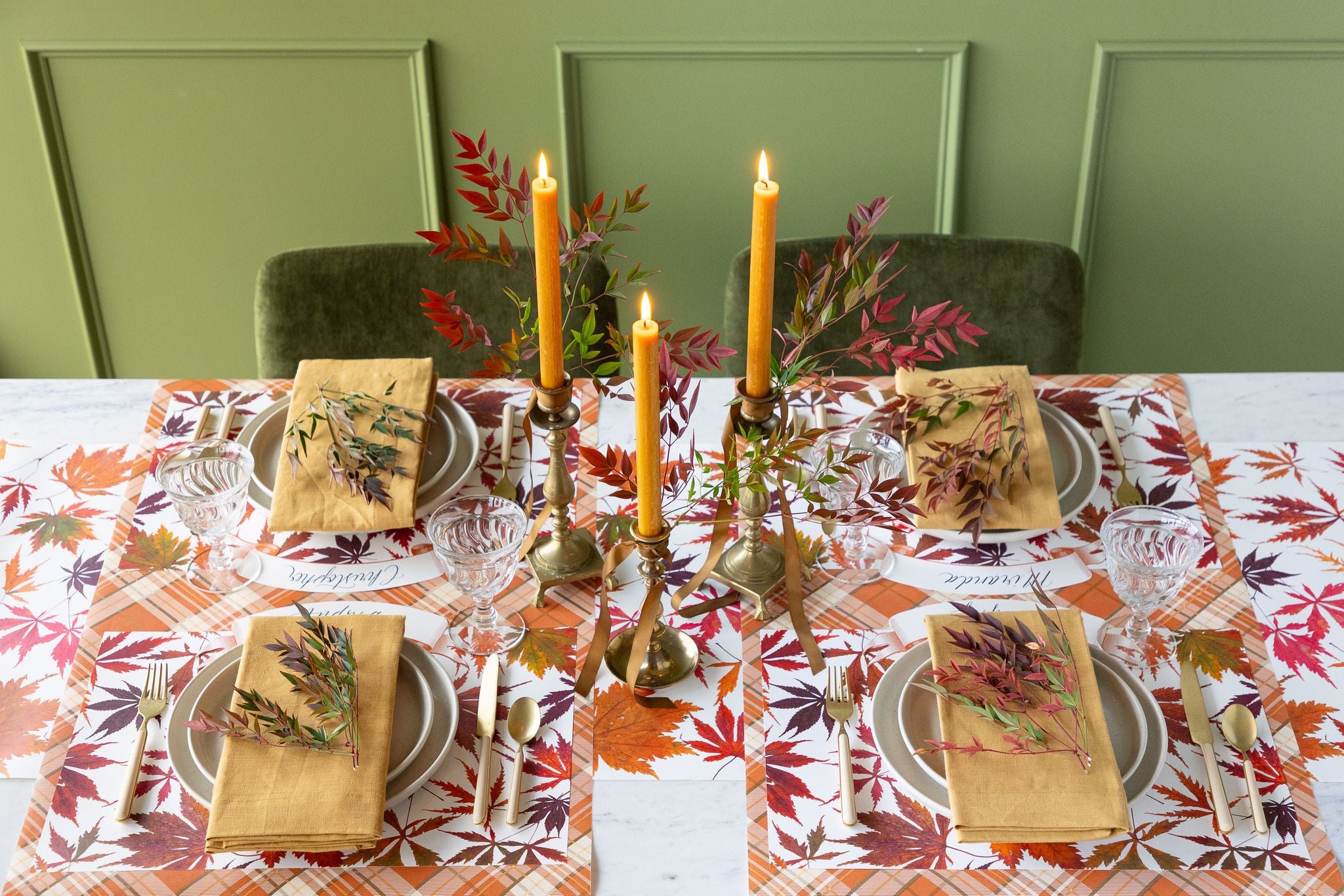 Set table with fall-themed decor, including place settings, candles, and a patterned tablecloth.