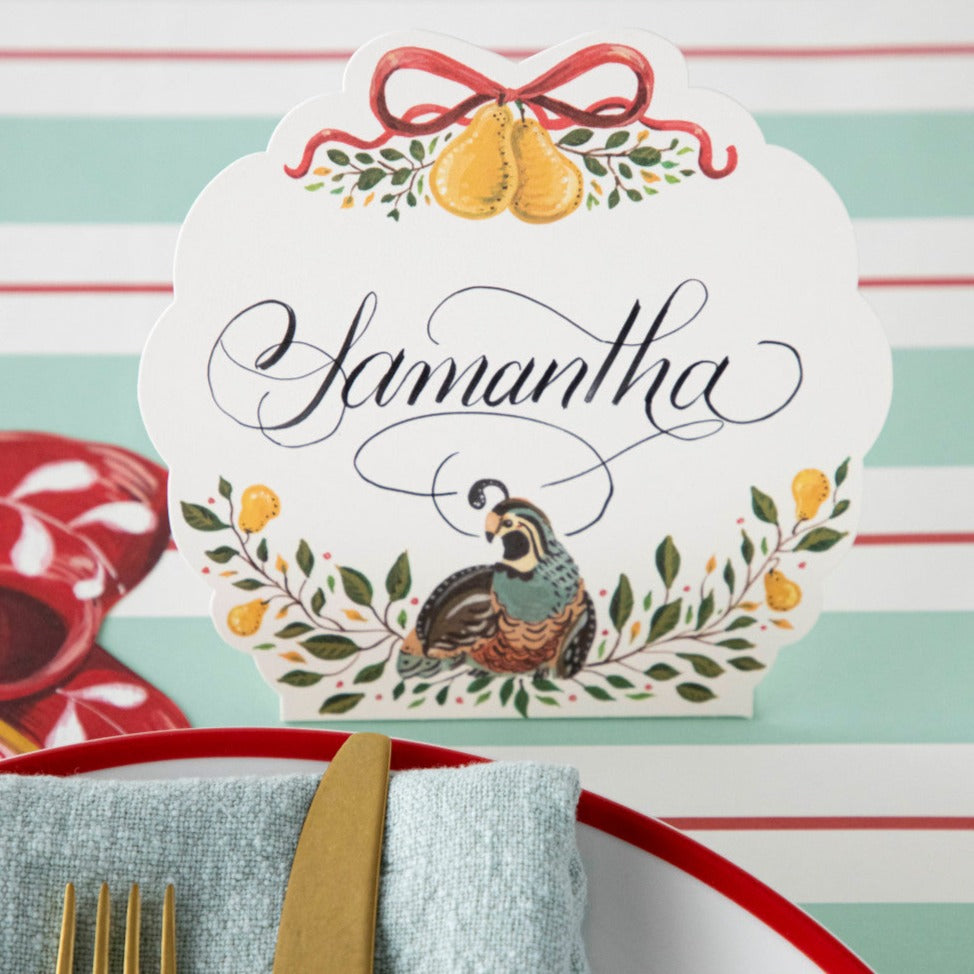 Close-up of a Partridge Place Card labeled &quot;Samantha&quot; standing behind the plate of an elegant Christmas place setting.