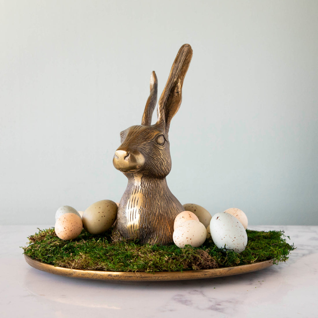 An Accent Decor Hare Platter sits on a bronze platter, surrounded by eggs and moss.