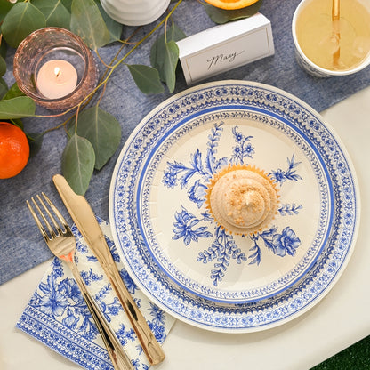 A Blue French Toile Paper Party Dinnerware table setting with a cupcake and oranges by Coterie Party Supplies.