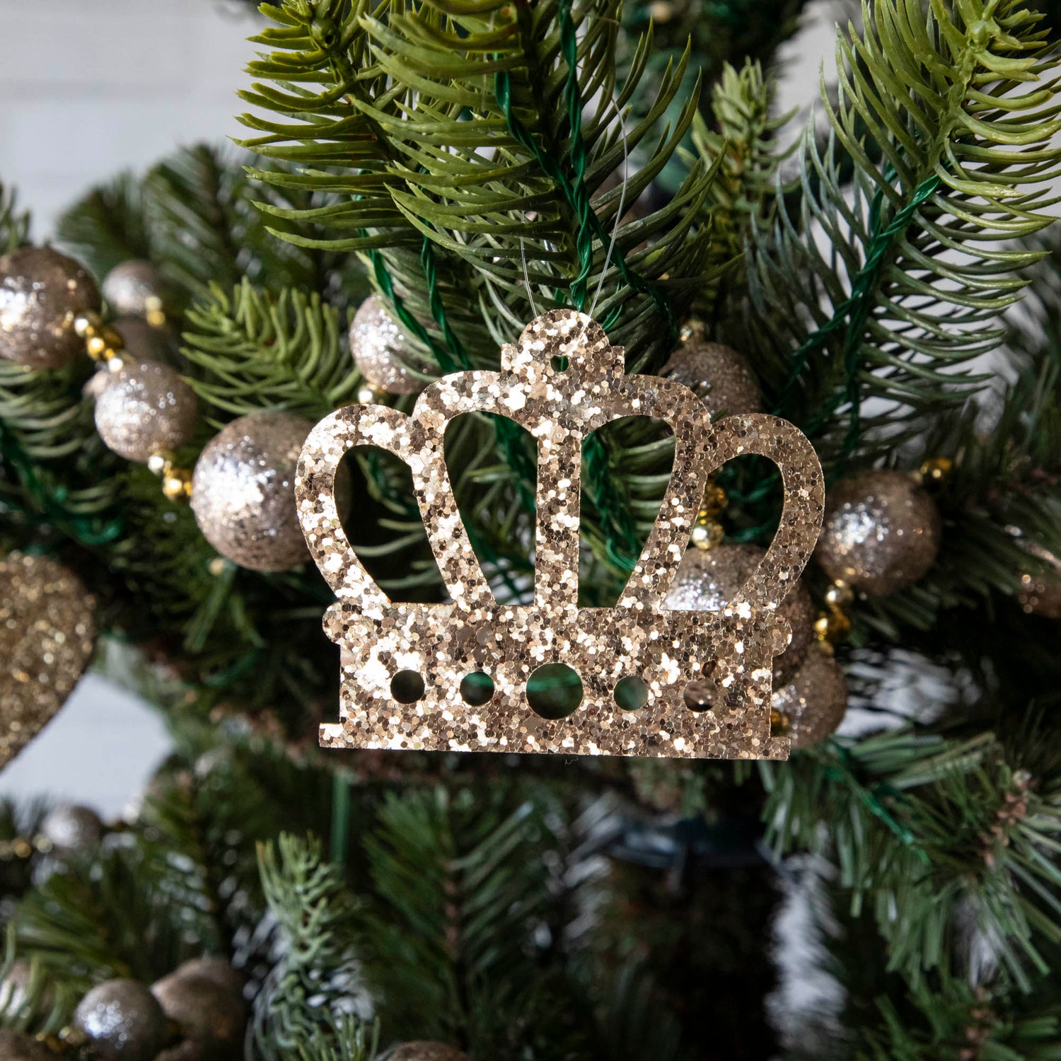 Gold glitter crown-shaped ornament hanging on a Christmas tree.