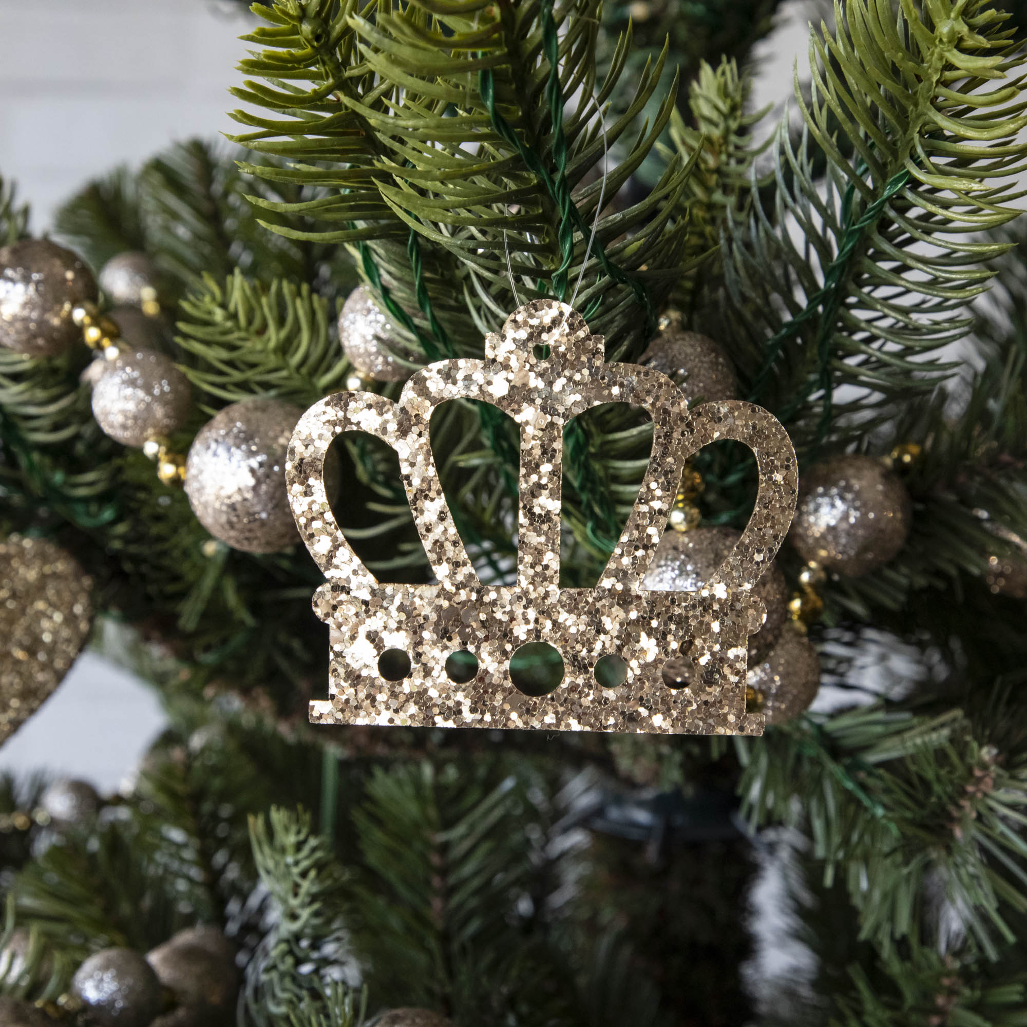 Gold glitter crown-shaped ornament hanging on a Christmas tree.