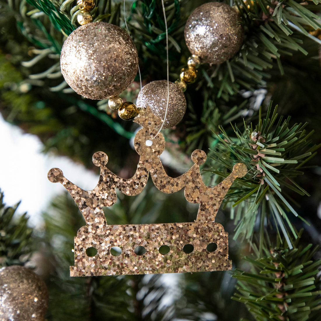 Gold glitter crown-shaped ornament hanging on a Christmas tree.