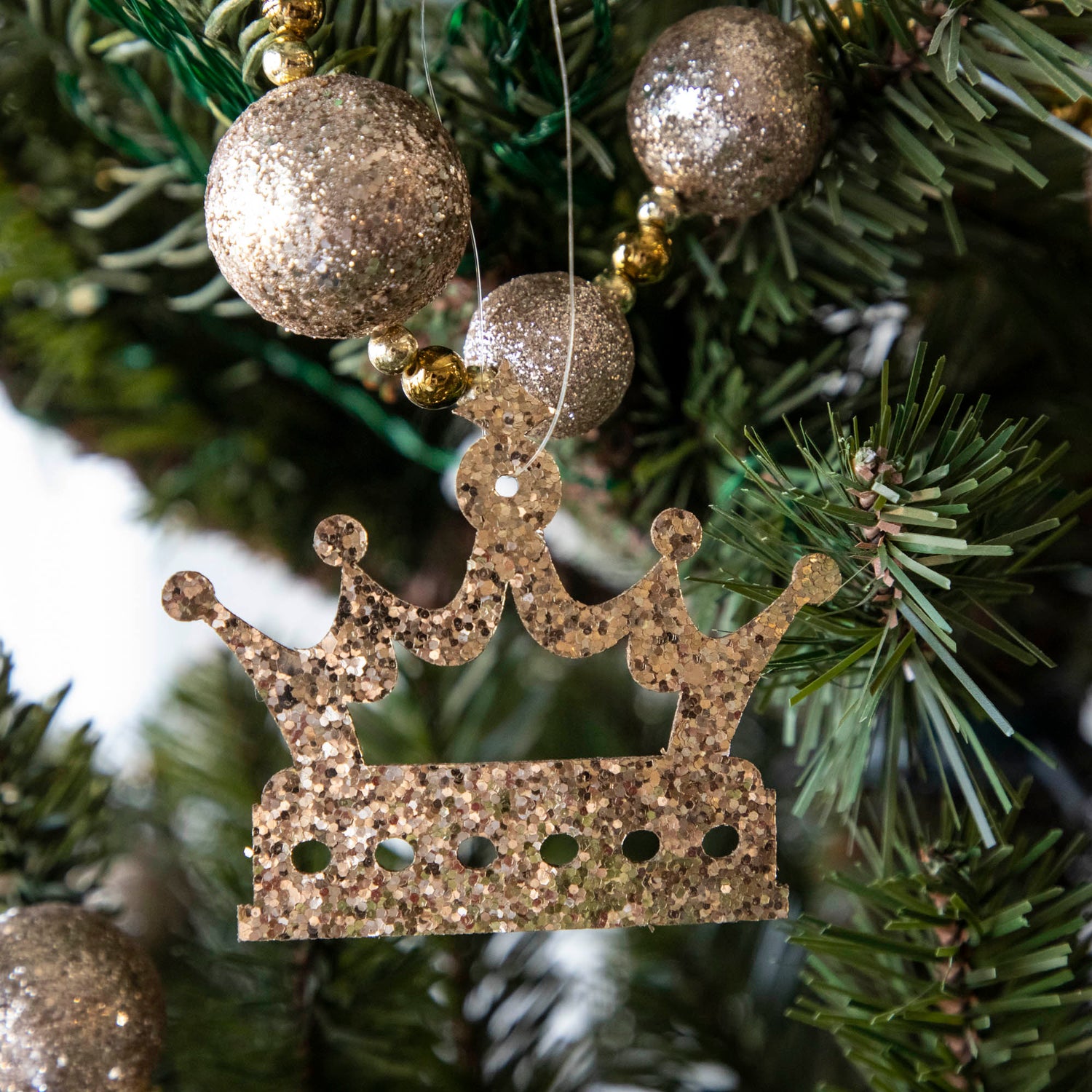 Gold glitter crown-shaped ornament hanging on a Christmas tree.