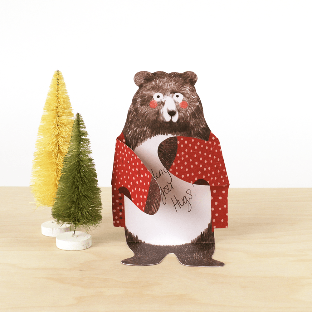 A Bear Hugs Notecards with a bear on it next to a Christmas tree by Chronicle Books.