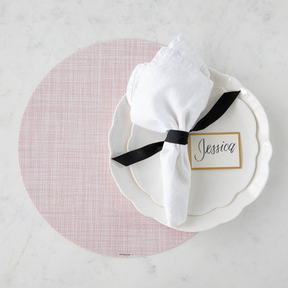 Elegant table setting with a floral theme, featuring pink and white dishes, gold cutlery, Chilewich Blush Mini Basketweave Mats, and personalized name card.