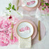 Elegant table setting with a floral theme, featuring pink and white dishes, gold cutlery, Chilewich Blush Mini Basketweave Mats, and personalized name card.