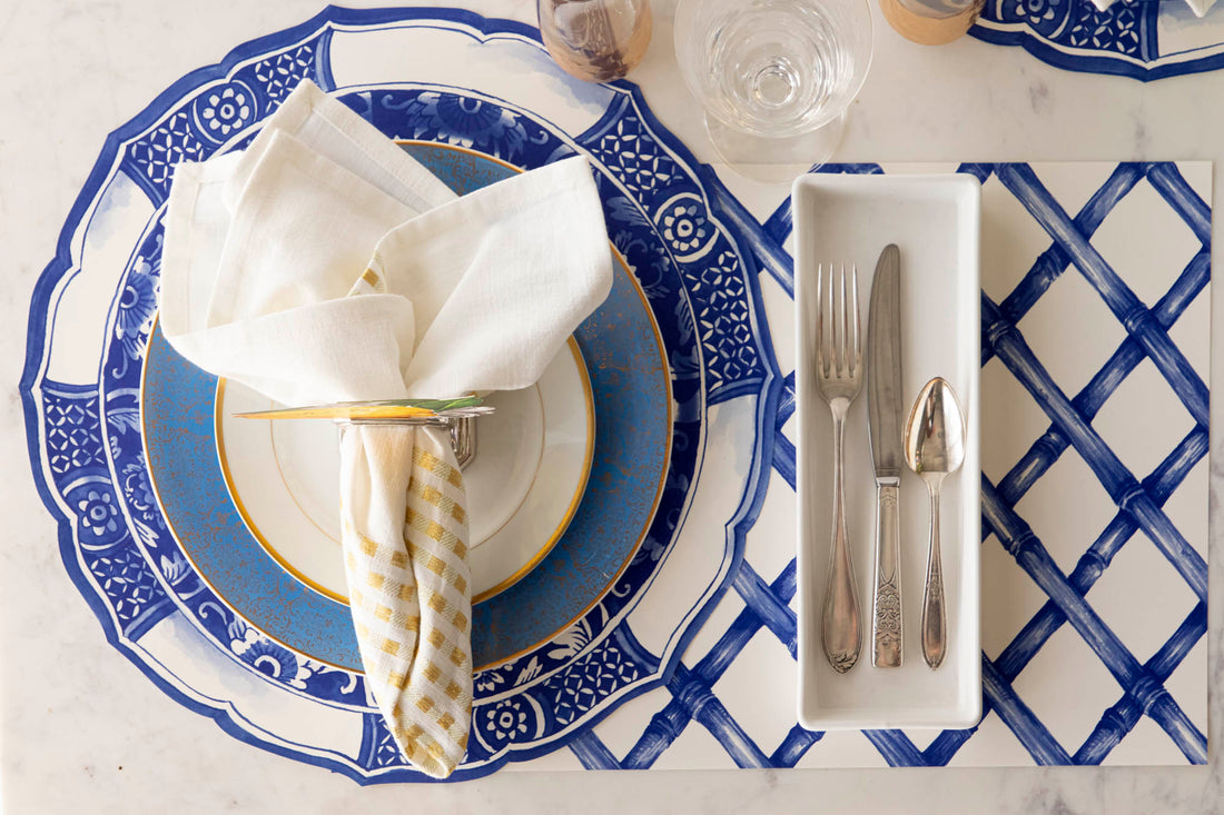 A blue and white place setting with silverware and a napkin on a Hester &amp; Cook Blue Lattice Placemat.