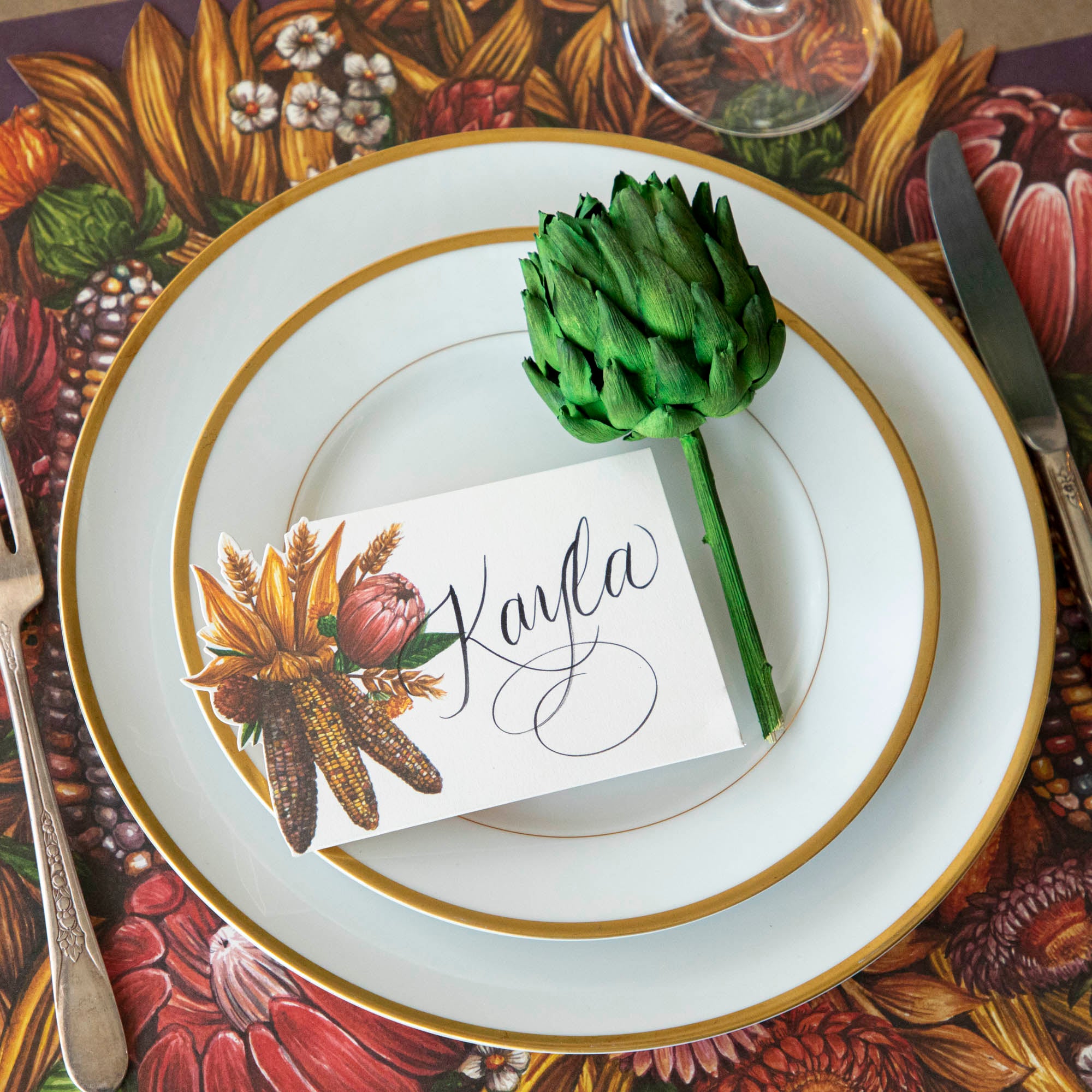 Place setting at a table with a single dried green artichoke next to a place card