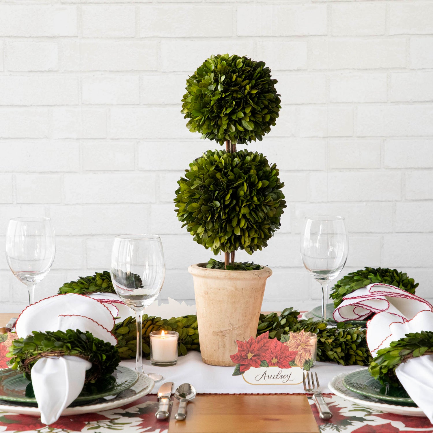 A Christmas table setting with a Mills Floral Company Preserved Boxwood Double Ball Topiary in a pot.