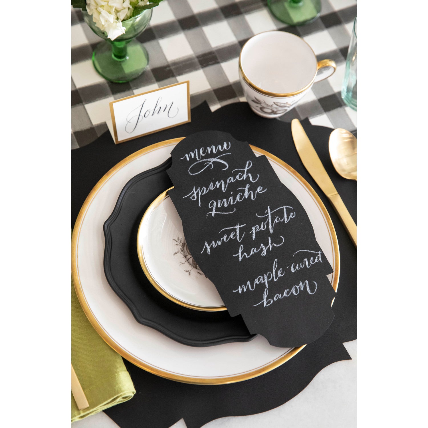 An elegant place setting featuring a Black Frame Table Accent resting on the plate with a menu hand-written in white script.