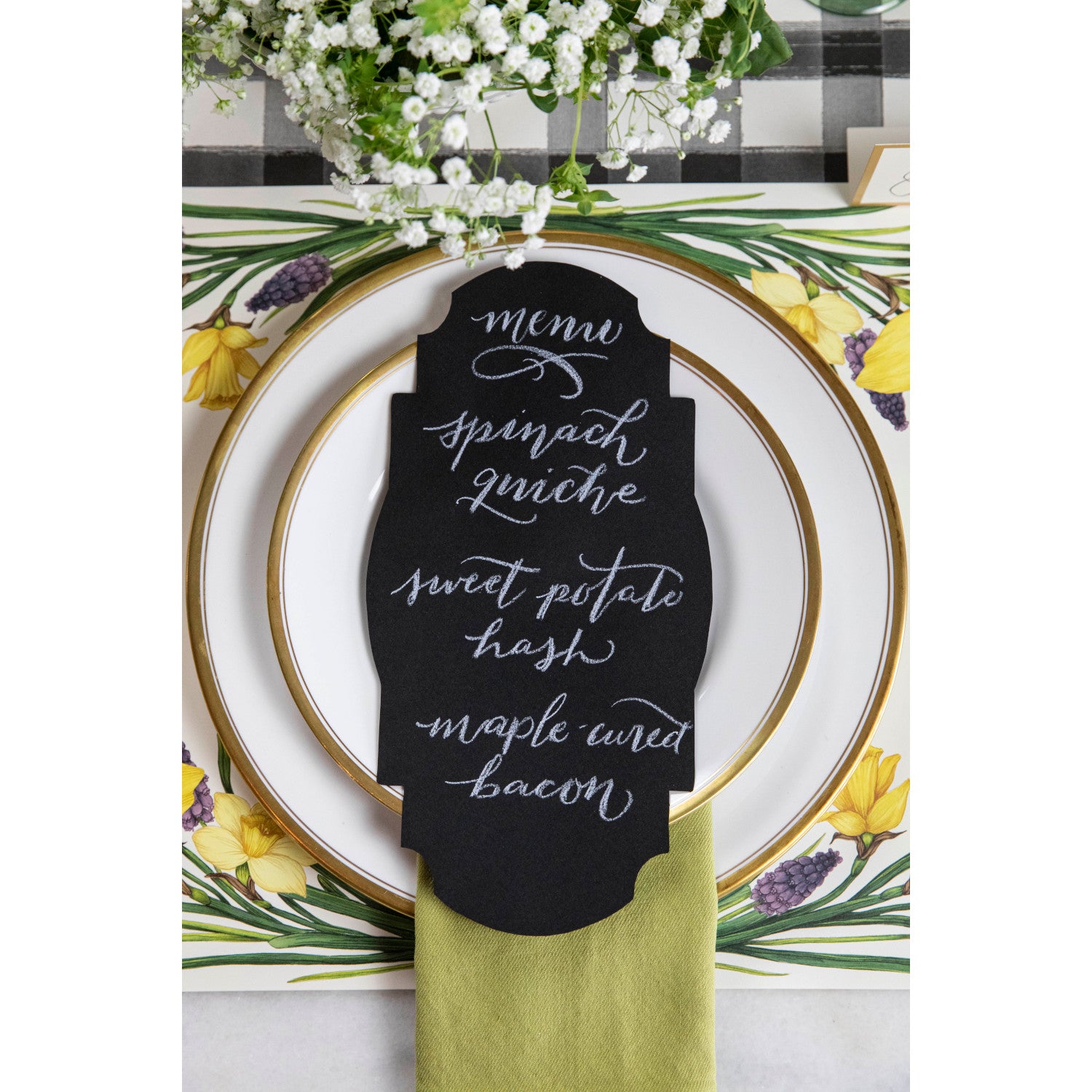 Top-down view of an elegant place setting featuring a Black Frame Table Accent resting on the plate with a menu hand-written in white script.