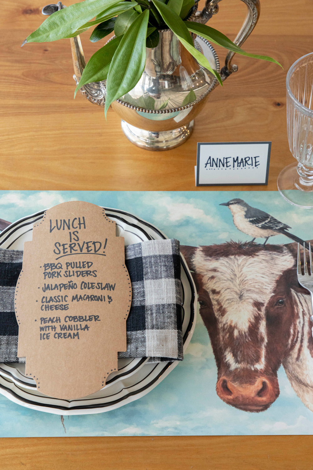 A place setting of the Buford &amp; Agnes Placemat with a Kraft Frame Table Card with the menu written on it. 