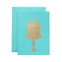 A turquoise-blue card with the silhouette of a birthday cake on a stand in solid gold leaf.