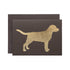 A dark brown card with the silhouette of a labrador-shaped dog with antlers in solid gold leaf.