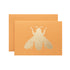 A bright orange card featuring the silhouette of a bee in solid gold leaf.