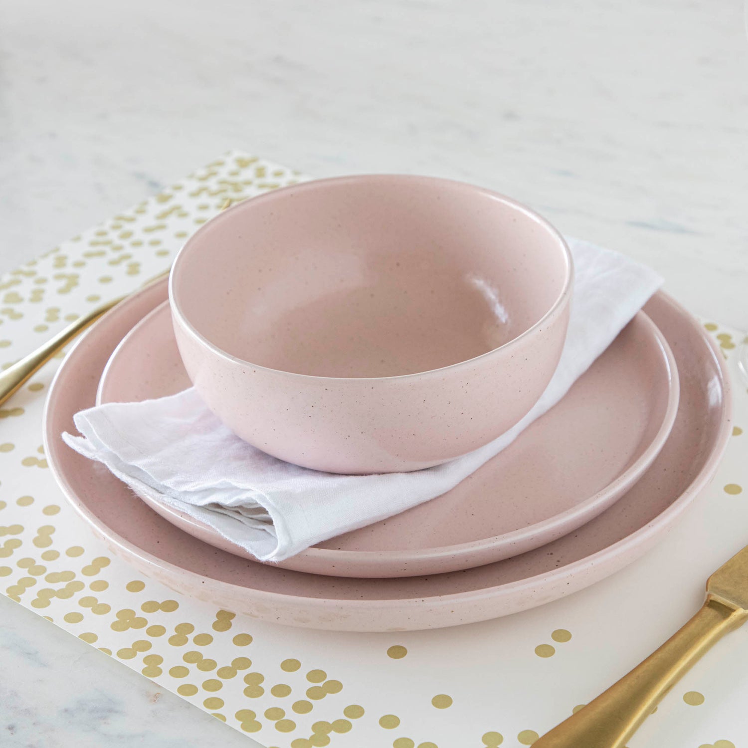 A fine stoneware Casafina Living Pacifica Marshmallow dinner set with a matte finish and gold polka dots on a table.