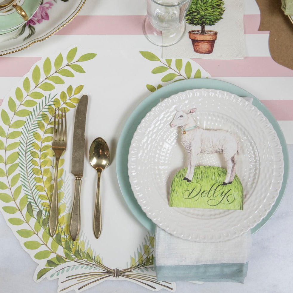 A table setting with a Little Lamb Place Card by Hester &amp; Cook on it, adorned with an Easter Garden Story theme.