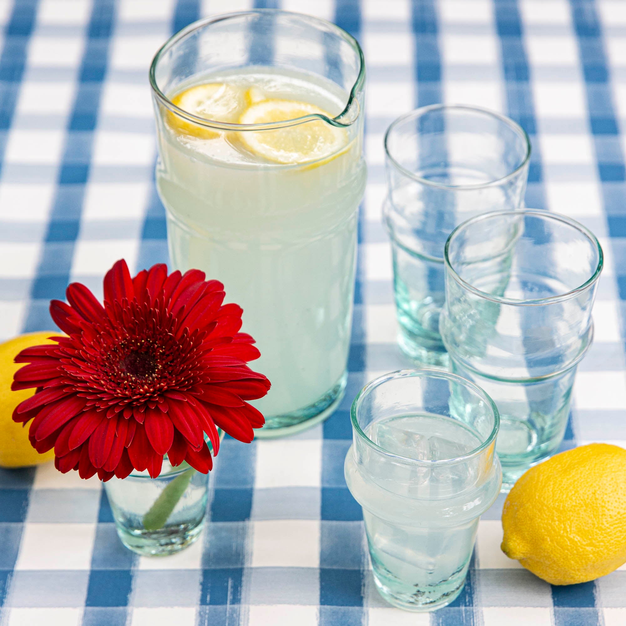 A pitcher of lemonade in a Clear Beldi Glassware on a blue and white checkered tablecloth.
