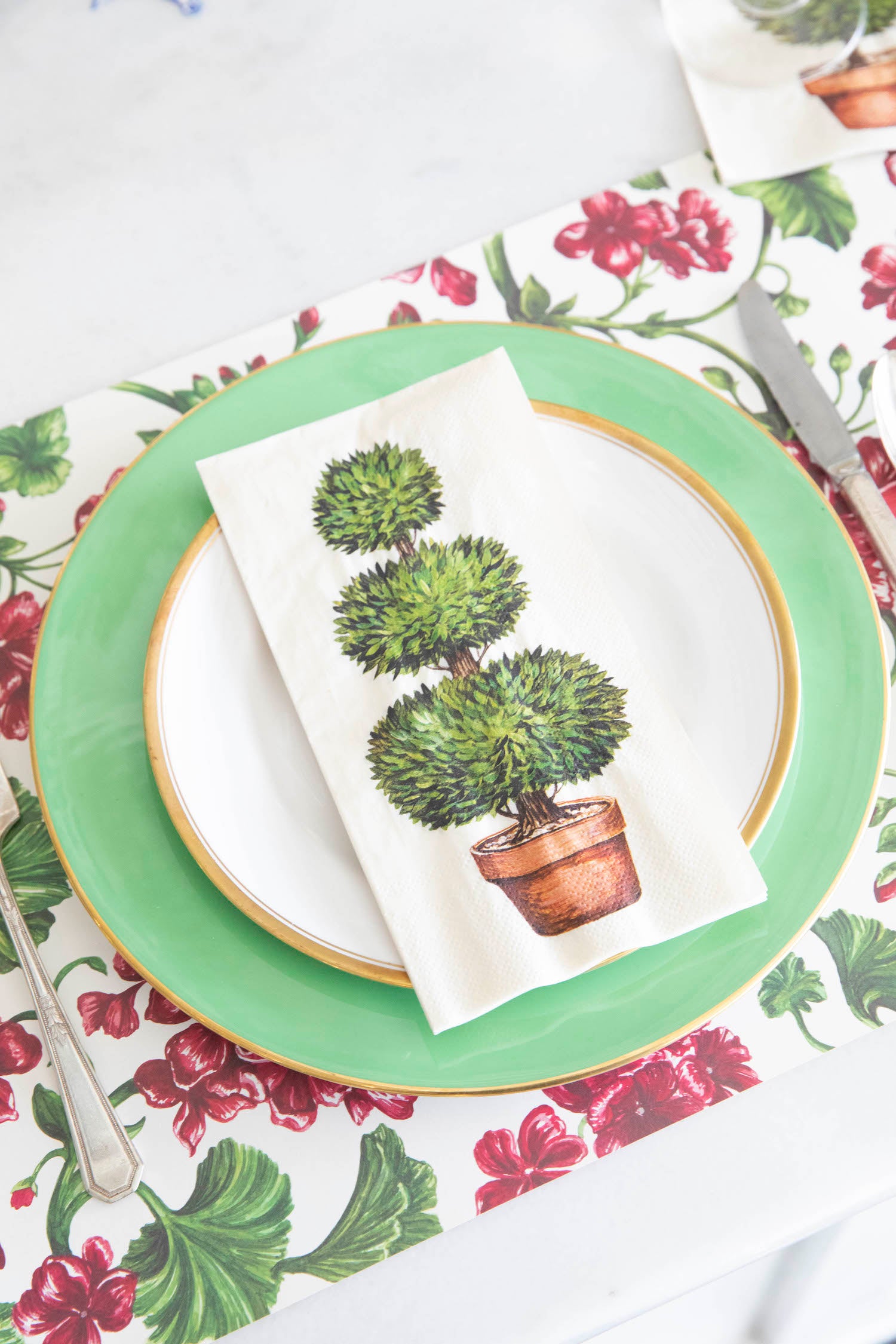 A party table setting with a green tablecloth, a green placemat, and Hester &amp; Cook Topiary Napkins.
