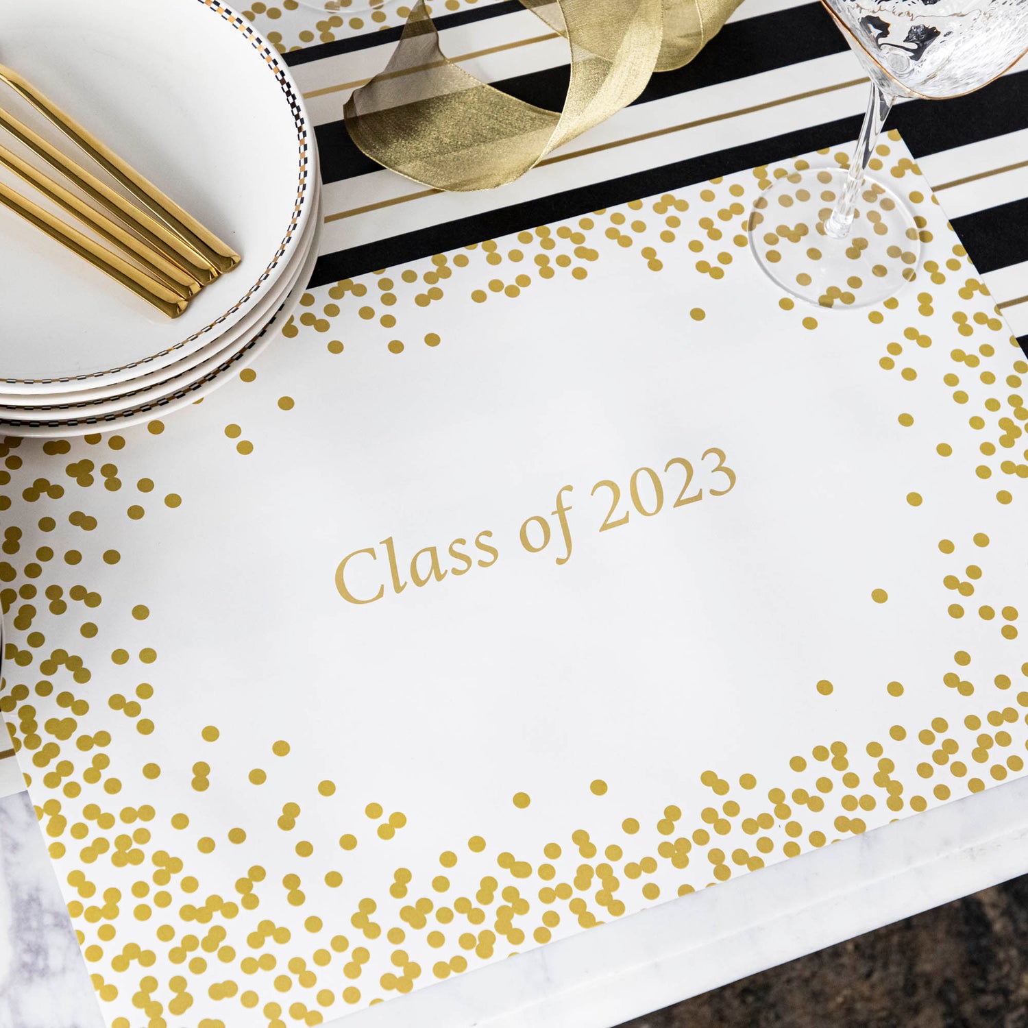 Table setting with Gold Confetti Placemat with personalized message printed in gold color: &quot;Class of 2023&quot;.