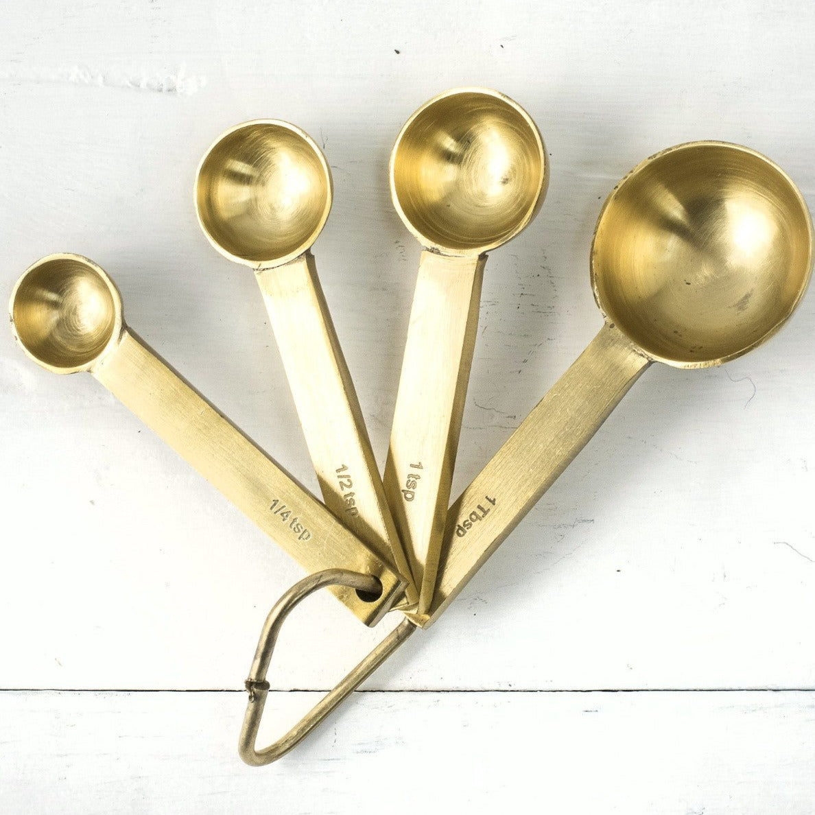A set of ethically crafted Be Home brass measuring spoons with a food-safe coating on a wooden surface.