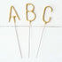 Three Tops Malibu gold Letter Sparklers on a wooden surface.