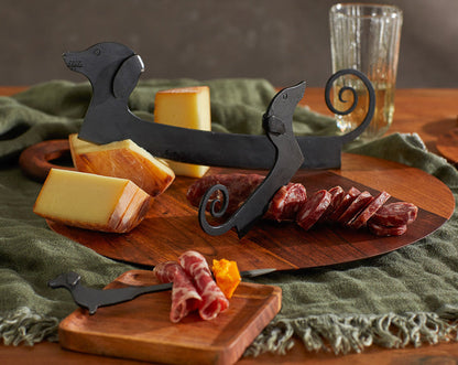 Metal cheese knives with Small Dachshund Rocking Cheese Slicer silhouettes among assorted cheese and meat slices.