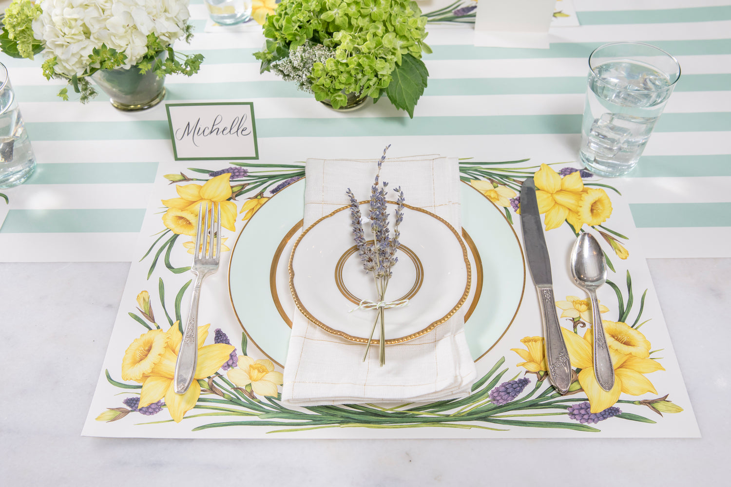 A spring table setting with Daffodil Placemats by Hester &amp; Cook on a striped tablecloth.