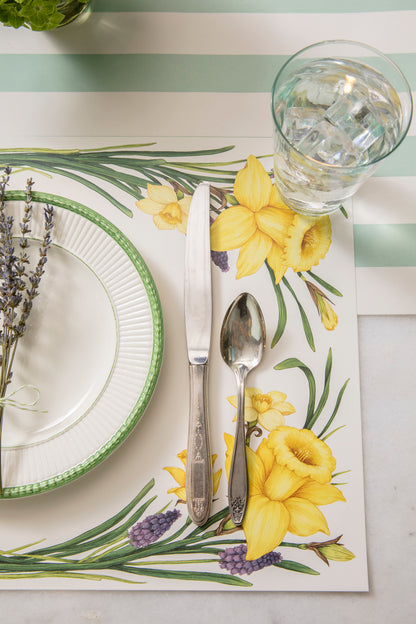 A Daffodil Placemat with a spoon and a glass of water on it, made by Hester &amp; Cook.