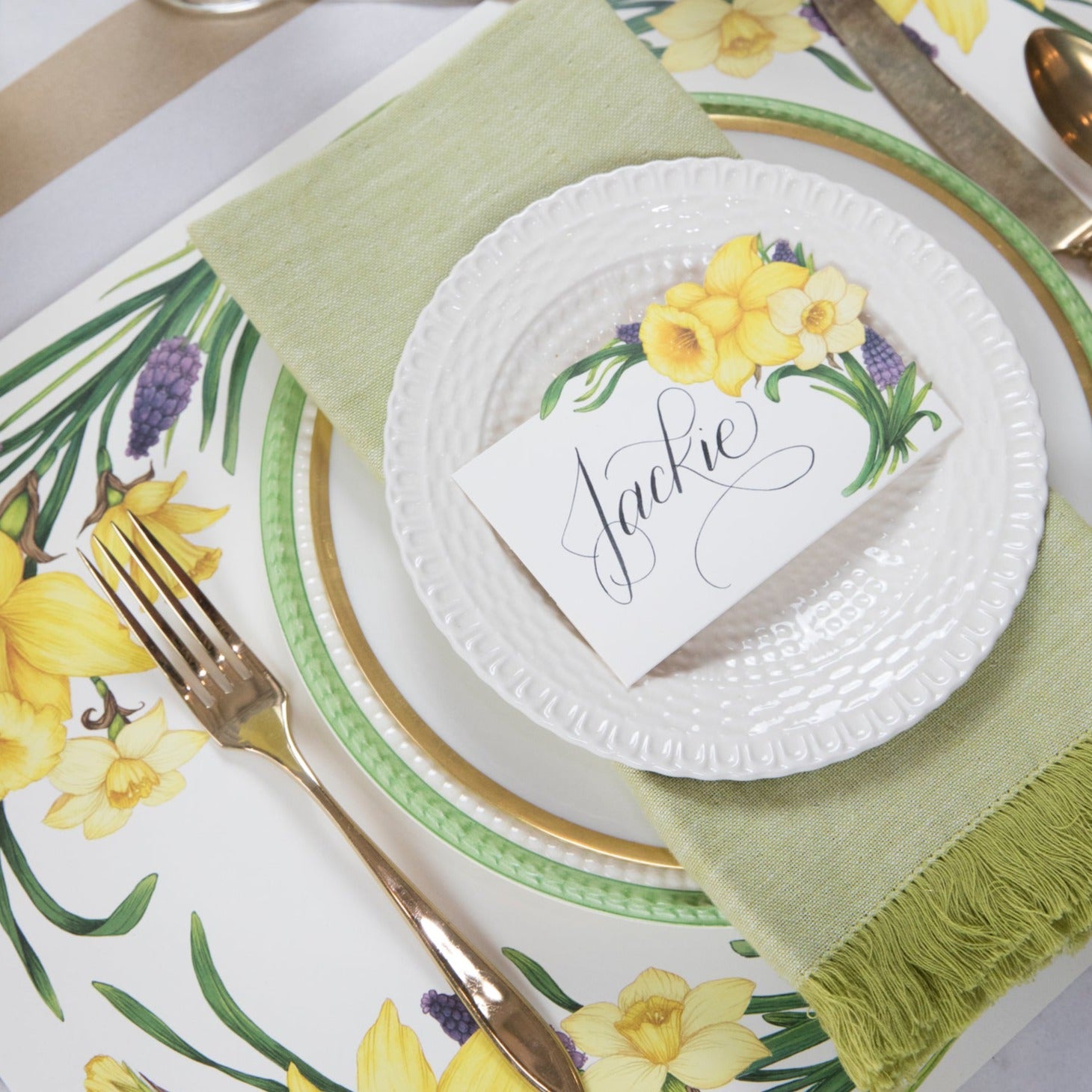 A Hester &amp; Cook Daffodil Place Card reading &quot;Jackie&quot; laying flat on a plate in an elegant place setting.