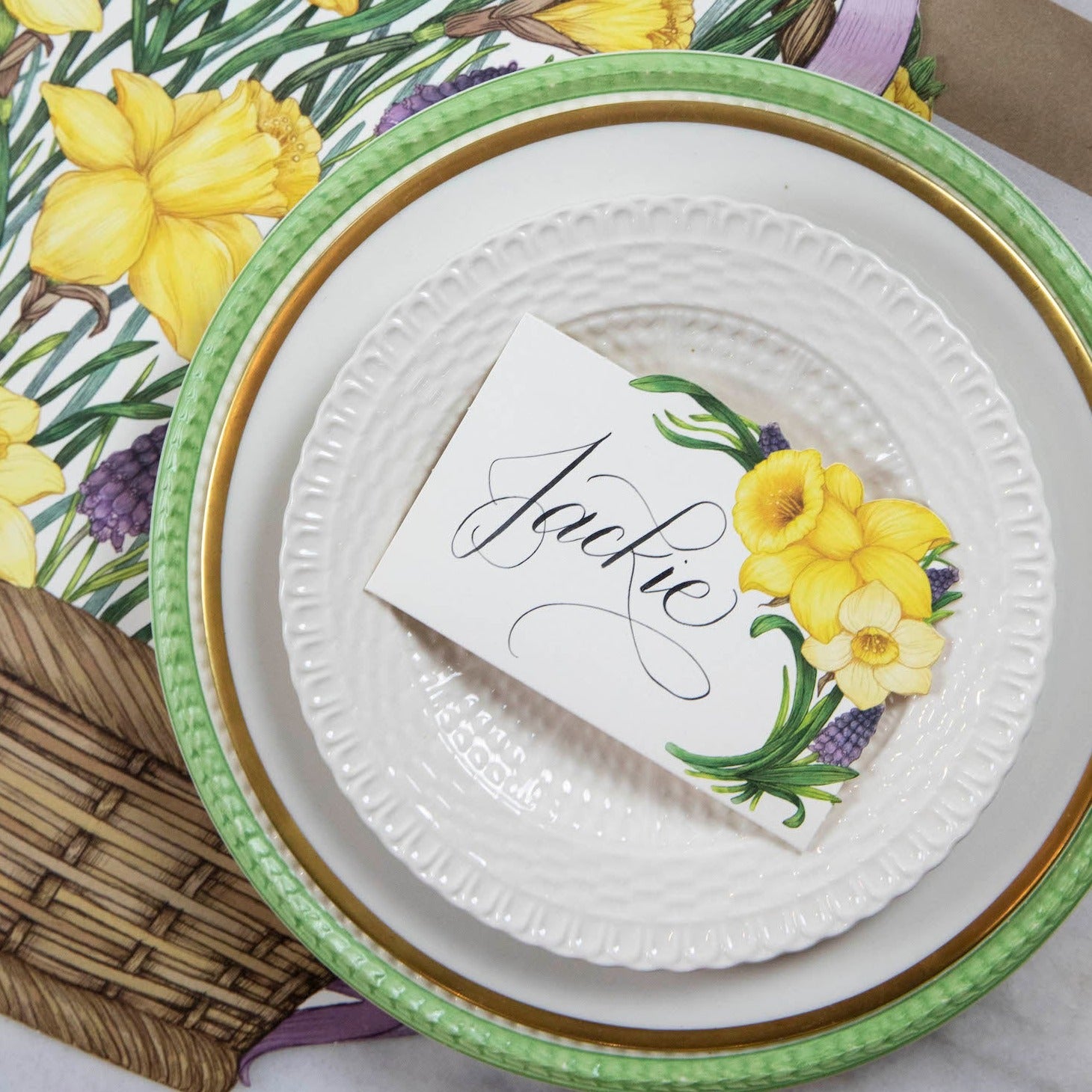 A Hester &amp; Cook Daffodil Place Card labeled &quot;Jackie&quot; laying flat on a plate in an elegant tablescape.