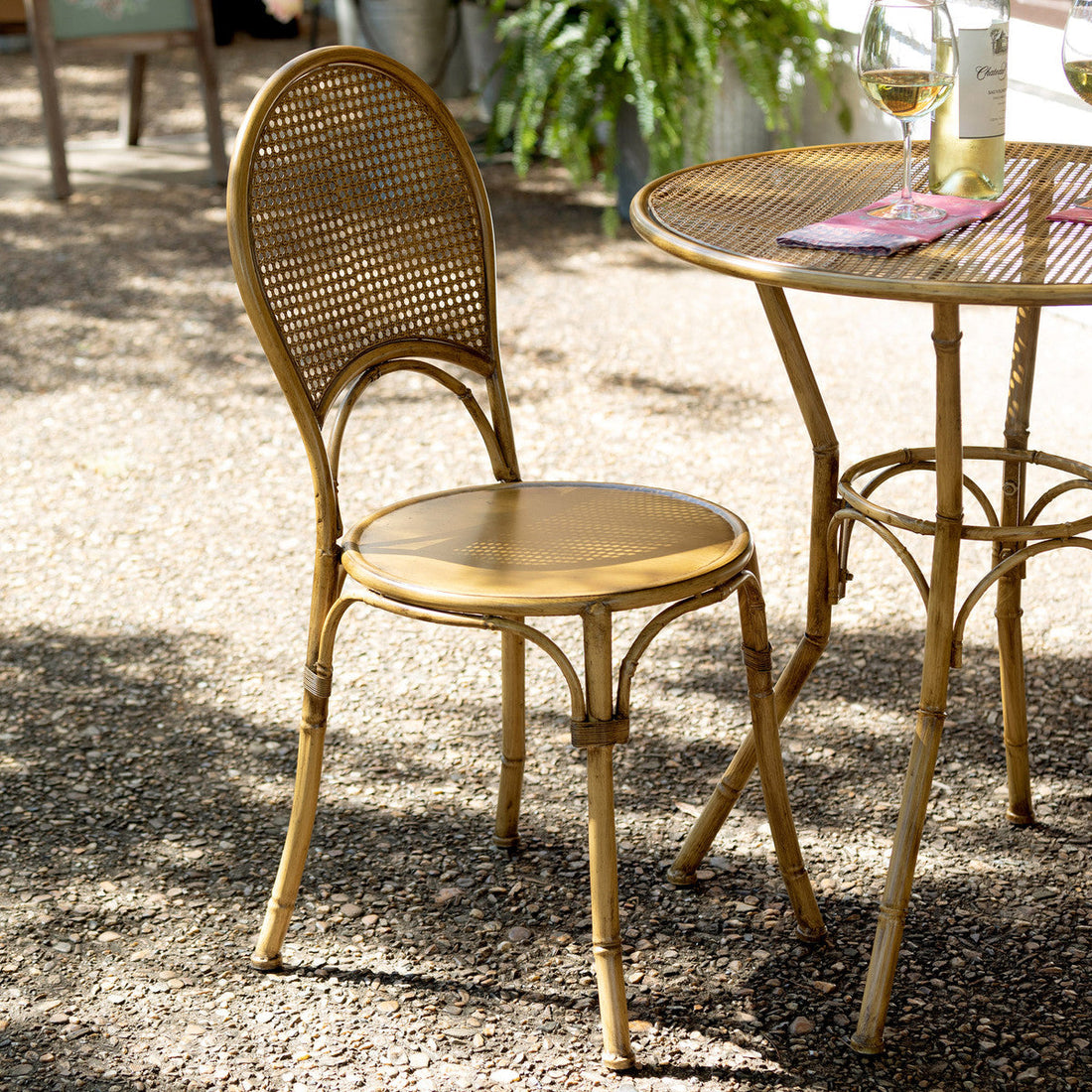 A Park Hill metal bamboo bistro chair near a table with a glass of white wine in an outdoor coastal living setting.