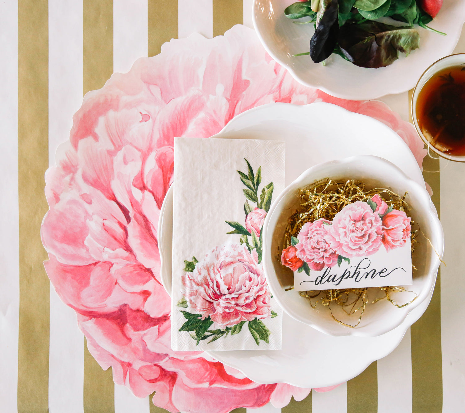 A table setting with fresh flowers, Pink Peony Napkins, on a gold striped tablecloth by Hester &amp; Cook.