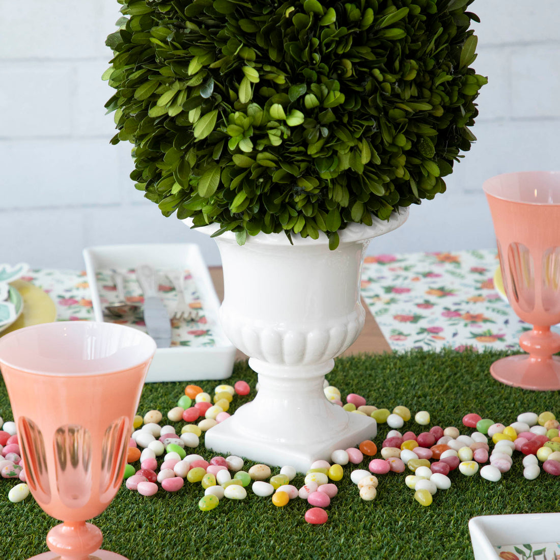 An easter table setting with a pink vase and candy, adorned with a Talking Tables Artificial Grass Table Runner centerpiece and party-themed table runner.