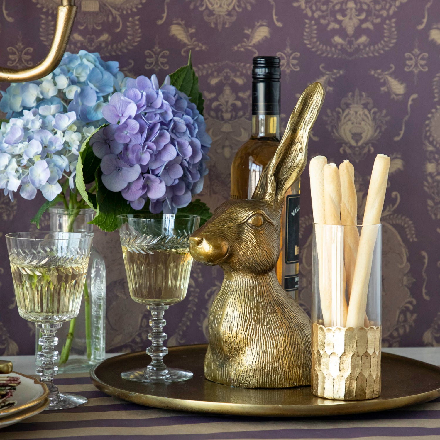 A whimsical gold Hare Platter perched on a bronze platter, elegantly displayed on a table alongside a glass of wine. (Brand: Accent Decor)
