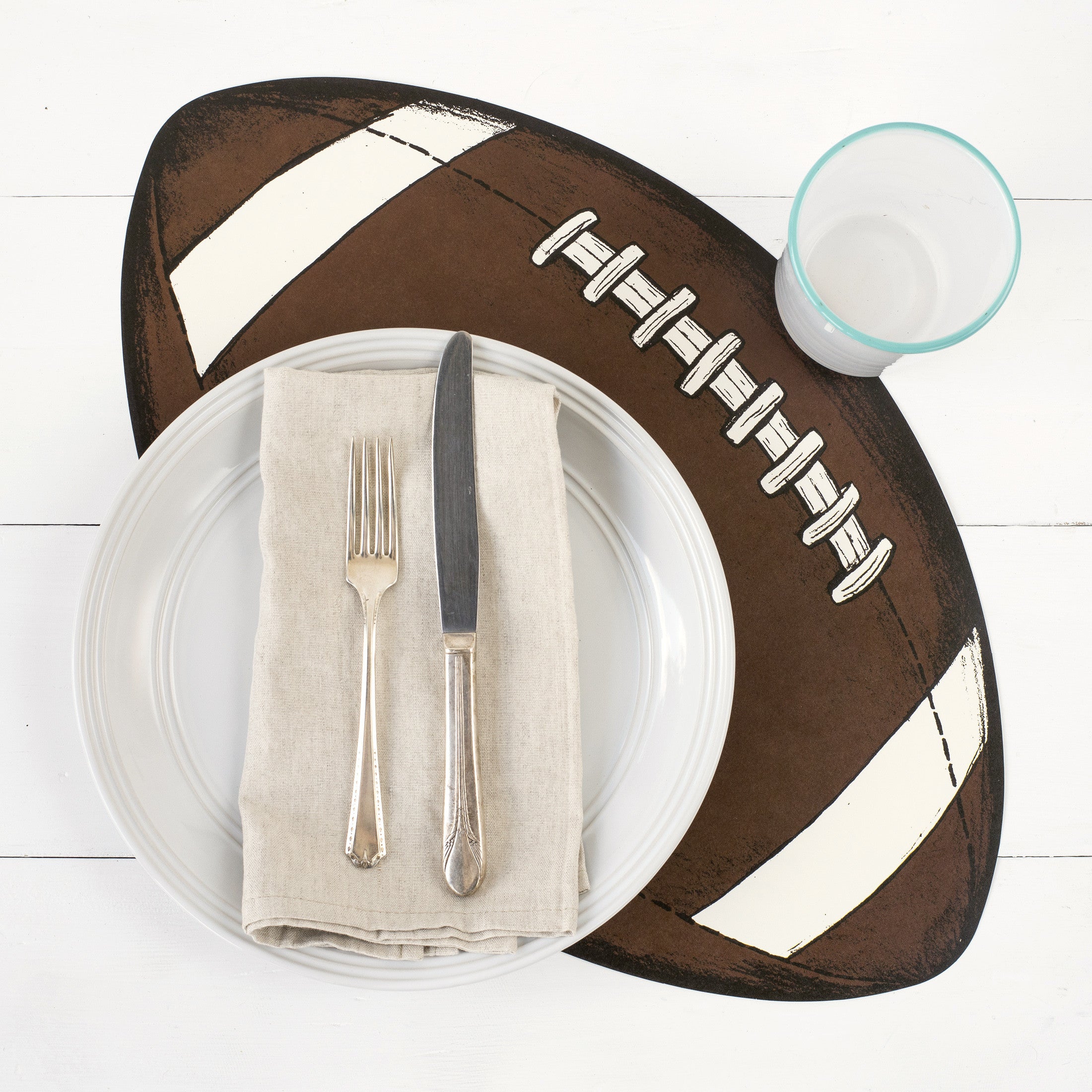 An Hester &amp; Cook die-cut football placemat with utensils on it, creating a festive tablescape.