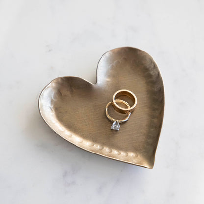 A HomArt Forged Iron Heart Tray with gold and silver rings on a copper-colored, pink, and white striped surface.