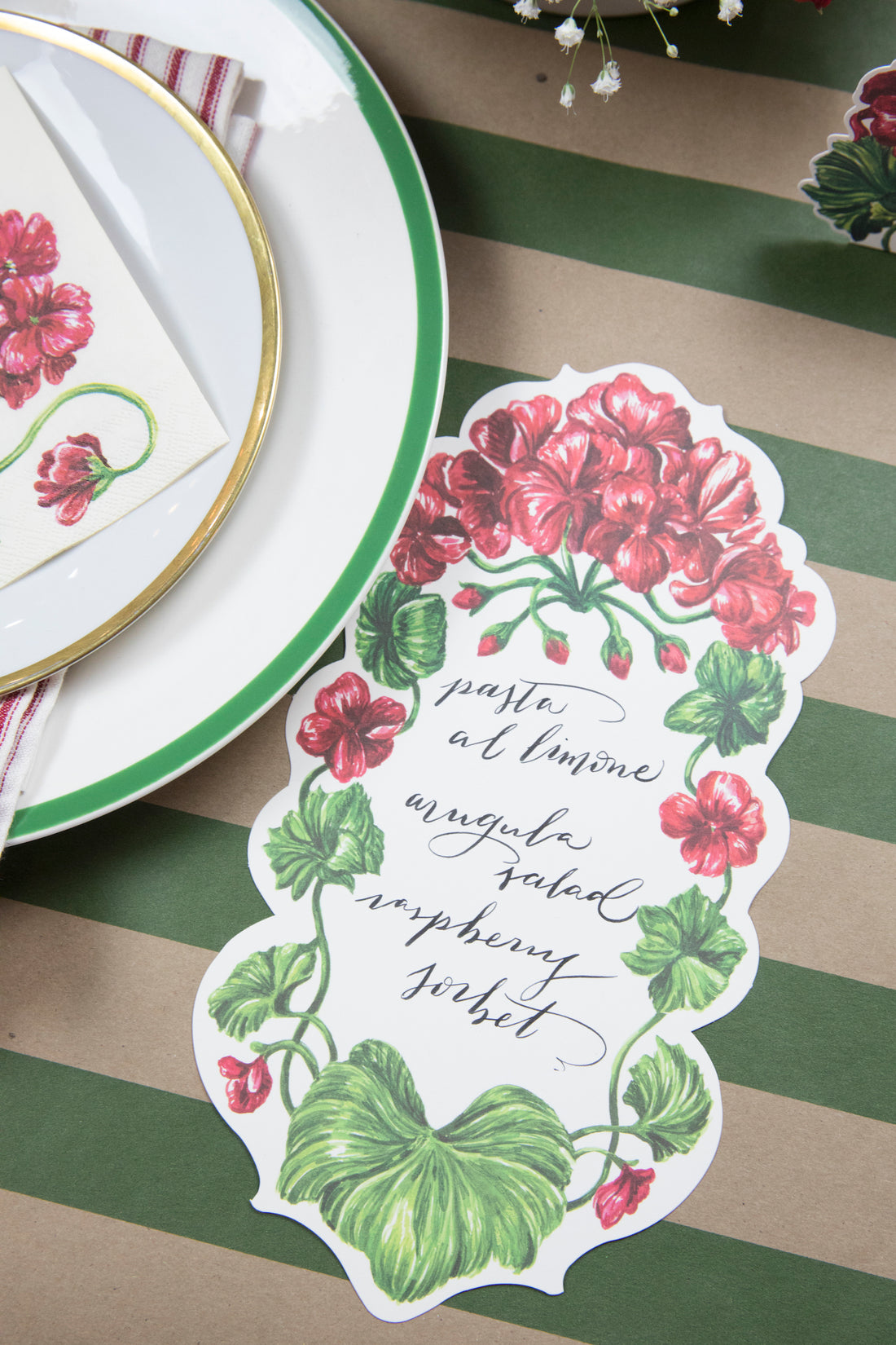 A Geranium Table Accent with a menu written on it in beautiful cursive resting next to the plate of an elegant table setting.