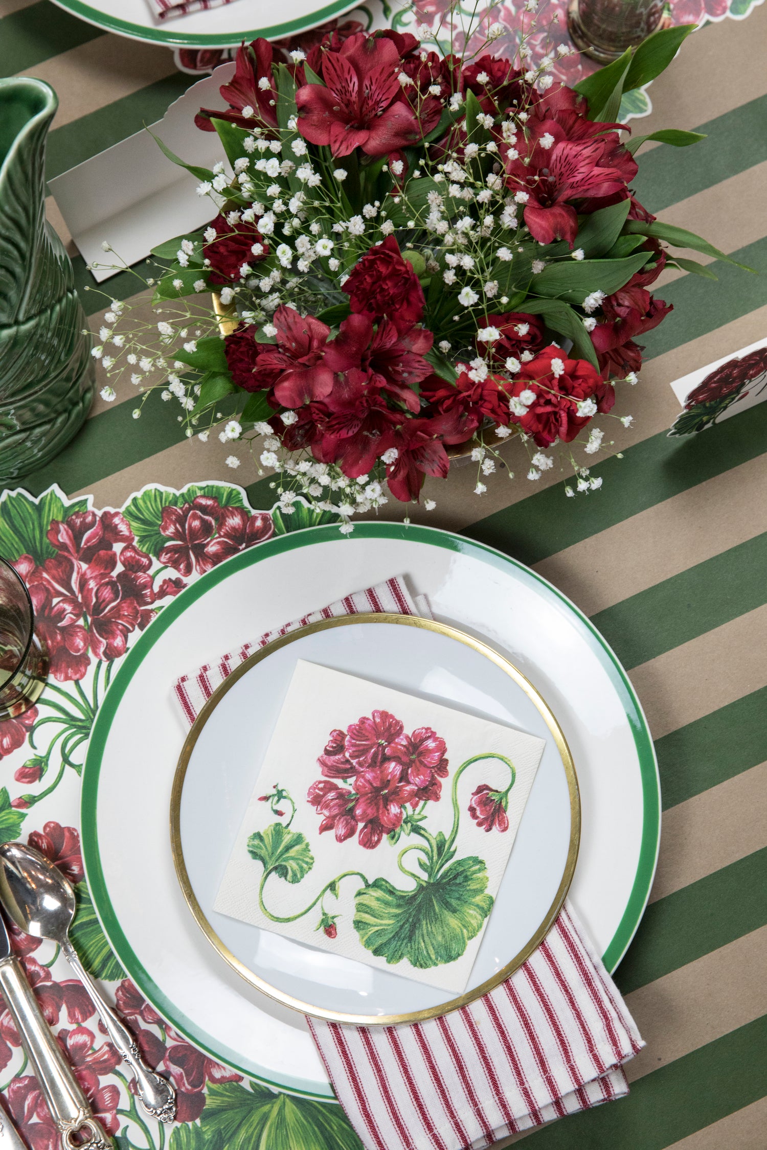 A summer table setting adorned with Hester &amp; Cook die-cut geranium placemats and a delightful mix of red, green, and white flowers.