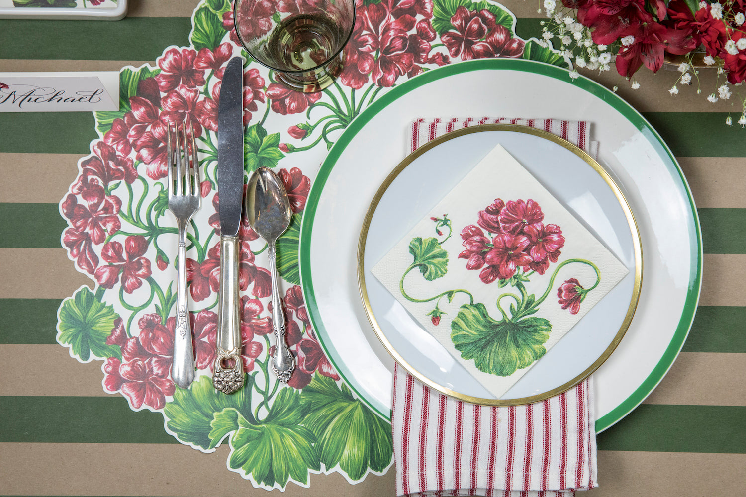 A red and green Die-cut Geranium Placemat by Hester &amp; Cook, perfect for adding a touch of summer florals to your table setting.