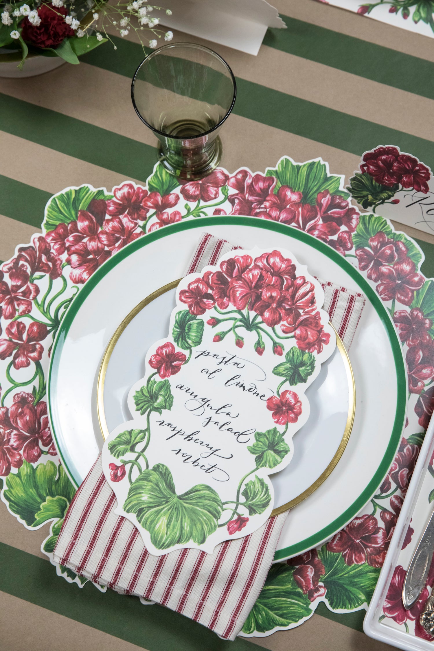 A Geranium Table Accent with a menu written on it in beautiful cursive resting on the plate of an elegant place setting.
