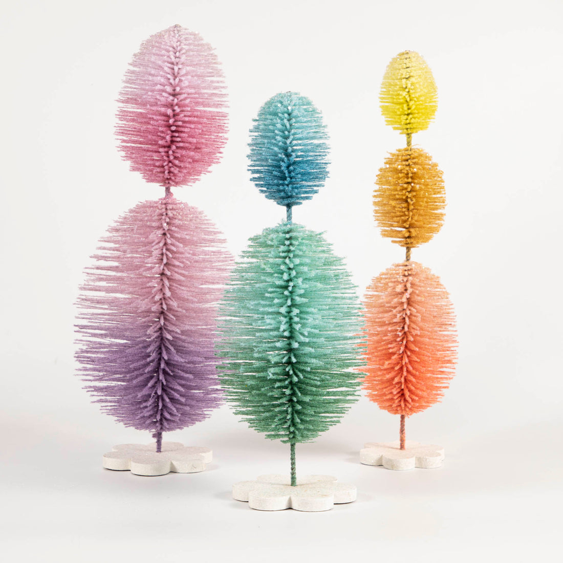 Three Glitterville Sisal Topiary Trees, reminiscent of spring and Easter celebration, on a white background.