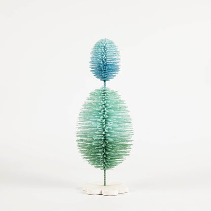 A Glitterville Sisal Topiary Tree, adorned in blue and green, stands on a white background, symbolizing an Easter celebration in the joyful season of spring.