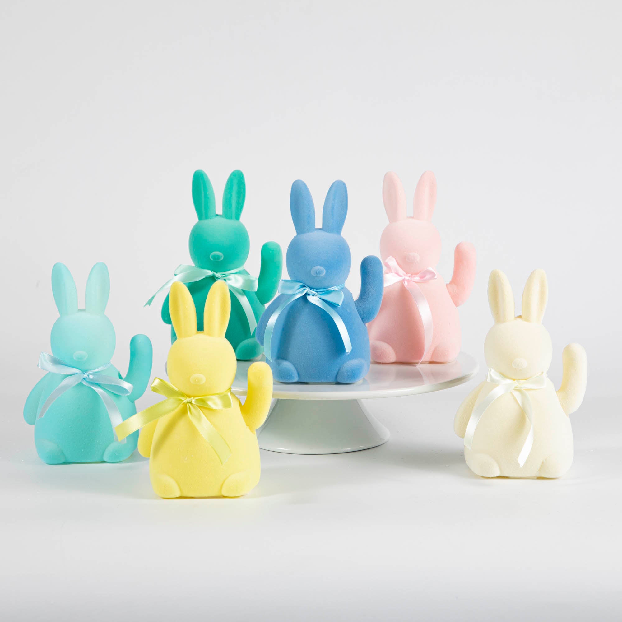 A group of Glitterville waving flocked bunny figurines on a white plate, perfect for the Easter season.