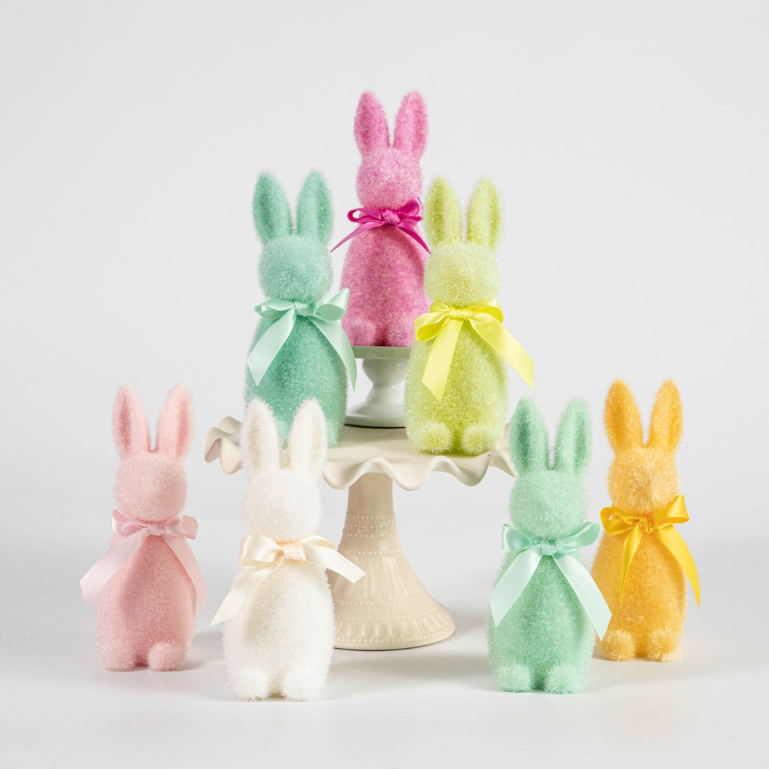 A group of Glitterville Small Flocked Pastel Button Nose Bunnies sitting on top of a cake stand.