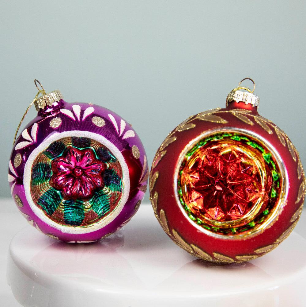 A close up of a red and purple Reflector ornament showing their intricate designs adorned with glitter and a colorful kaleidoscope inside.