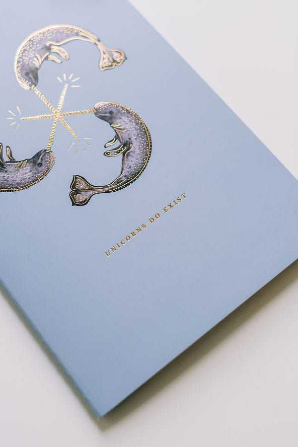A blue Narwhal Notebook Duo with a gold foiled narwhal fish on it from Good Juju Ink.