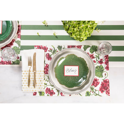 A table setting adorned with Geranium Garden Placemats by Hester &amp; Cook, and green and white plates, complemented by silverware.